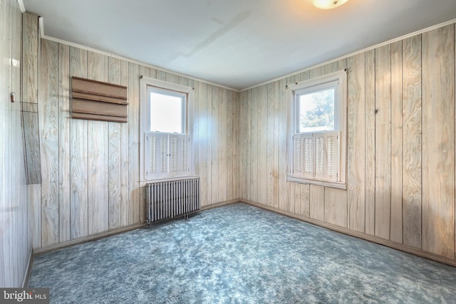 carpeted spare room with radiator heating unit, a healthy amount of sunlight, and wooden walls