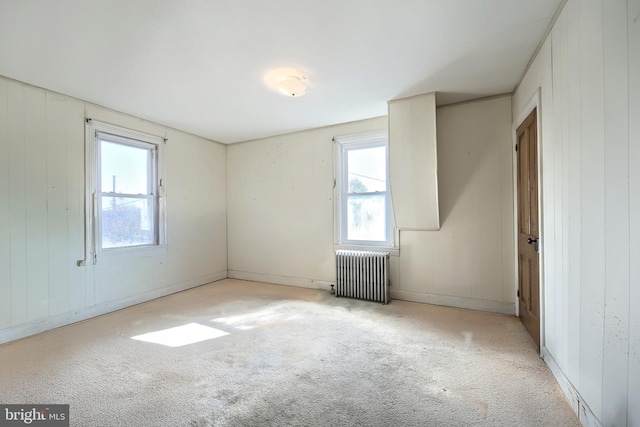 empty room with plenty of natural light, wooden walls, light colored carpet, and radiator