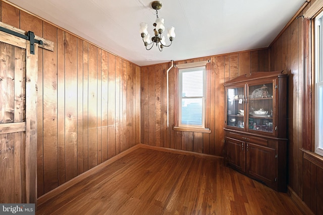 unfurnished dining area with wood walls, a chandelier, a barn door, and hardwood / wood-style floors