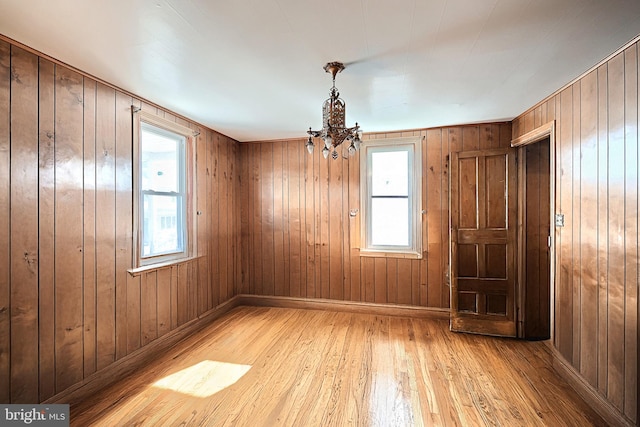 spare room featuring a chandelier, wooden walls, light hardwood / wood-style floors, and a healthy amount of sunlight