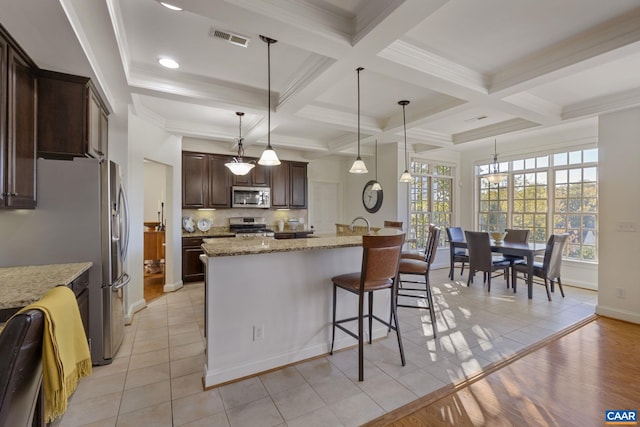 kitchen with hanging light fixtures, light stone countertops, light tile patterned flooring, stainless steel appliances, and coffered ceiling