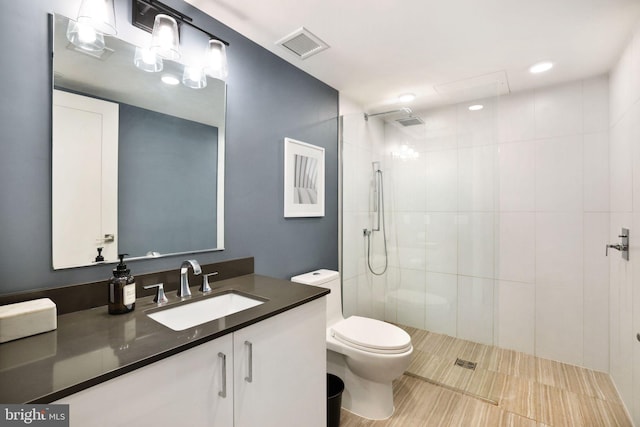 bathroom featuring toilet, vanity, and a tile shower