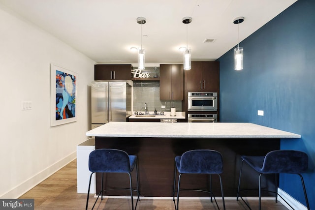 kitchen with dark brown cabinetry, a baseboard radiator, pendant lighting, and backsplash