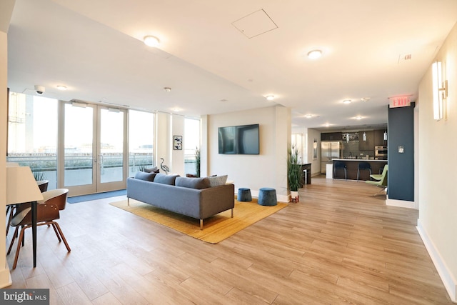 living room with light hardwood / wood-style floors, a wall of windows, and french doors