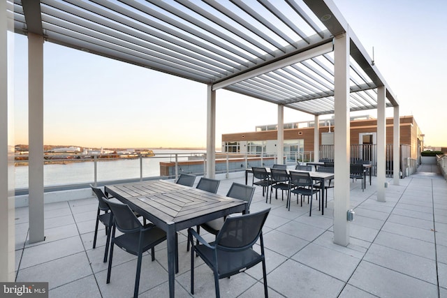 patio terrace at dusk featuring a water view and a pergola