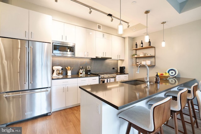 kitchen with high end appliances, white cabinets, hanging light fixtures, sink, and light hardwood / wood-style flooring