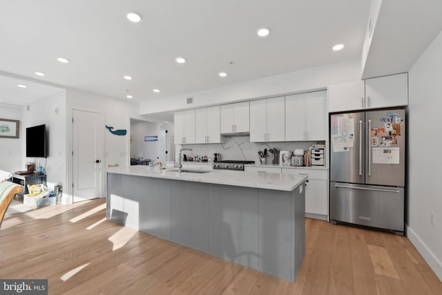 kitchen featuring a center island with sink, appliances with stainless steel finishes, white cabinetry, light hardwood / wood-style flooring, and sink