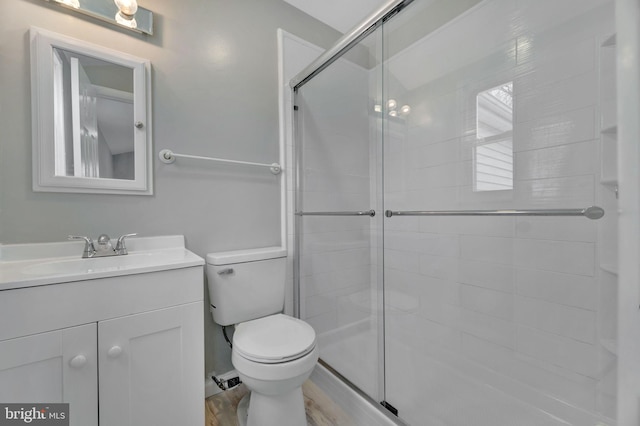 bathroom with a shower with door, vanity, hardwood / wood-style floors, and toilet