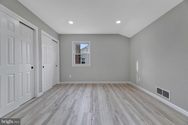 unfurnished bedroom with vaulted ceiling, two closets, and light wood-type flooring