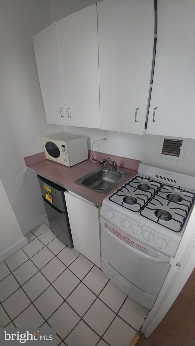 kitchen featuring white cabinets, light tile patterned floors, white appliances, and a sink
