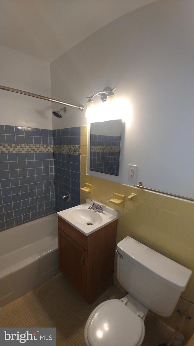 full bathroom with toilet, tile patterned flooring, vanity, tiled shower / bath combo, and tile walls