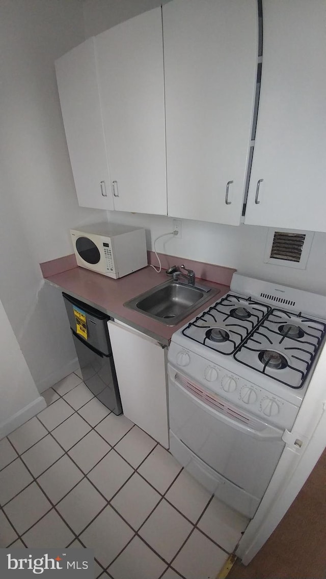 kitchen featuring white appliances, light tile patterned floors, sink, and white cabinets