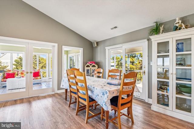 dining room featuring hardwood / wood-style flooring, french doors, a textured ceiling, and vaulted ceiling