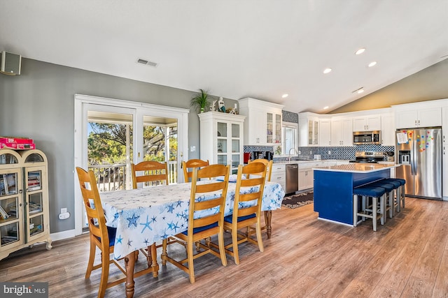 dining area featuring sink, light hardwood / wood-style flooring, and vaulted ceiling