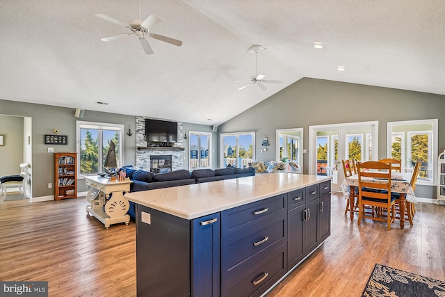 kitchen featuring a fireplace, ceiling fan, light hardwood / wood-style flooring, and a center island