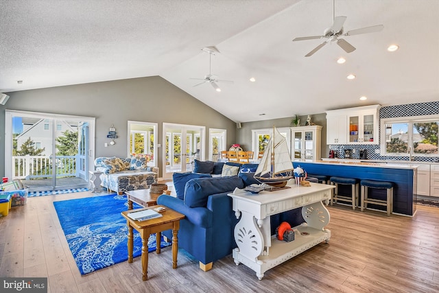 living room featuring ceiling fan, a textured ceiling, light wood-type flooring, and high vaulted ceiling