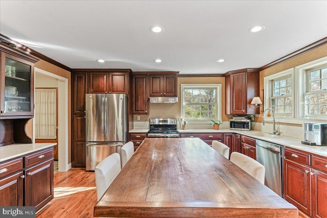 kitchen featuring a kitchen island, appliances with stainless steel finishes, ornamental molding, light hardwood / wood-style floors, and sink