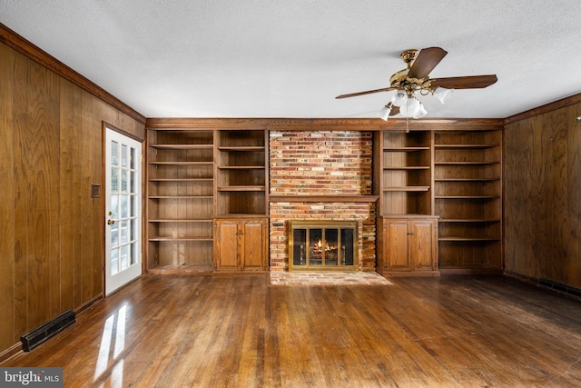 unfurnished living room featuring a brick fireplace, a textured ceiling, ceiling fan, wooden walls, and built in features