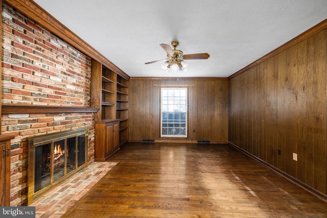 unfurnished living room featuring wooden walls, a fireplace, ceiling fan, and ornamental molding