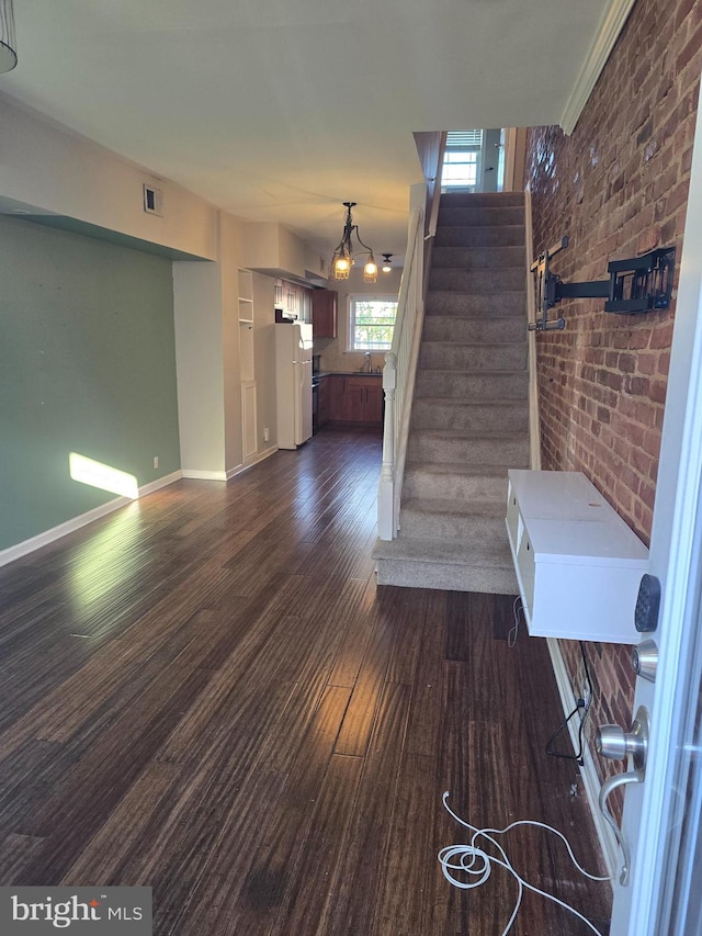 stairway with hardwood / wood-style flooring, a chandelier, brick wall, and sink