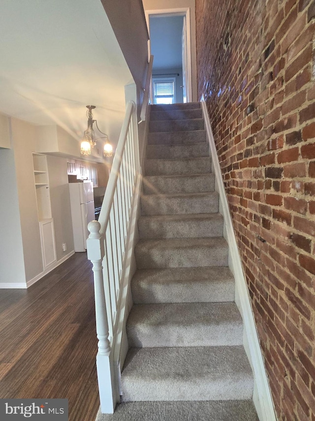 stairs with hardwood / wood-style flooring, brick wall, and an inviting chandelier