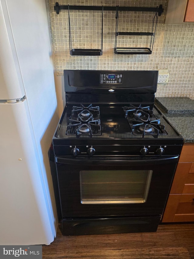 details featuring backsplash, dark hardwood / wood-style floors, white fridge, and black gas range oven