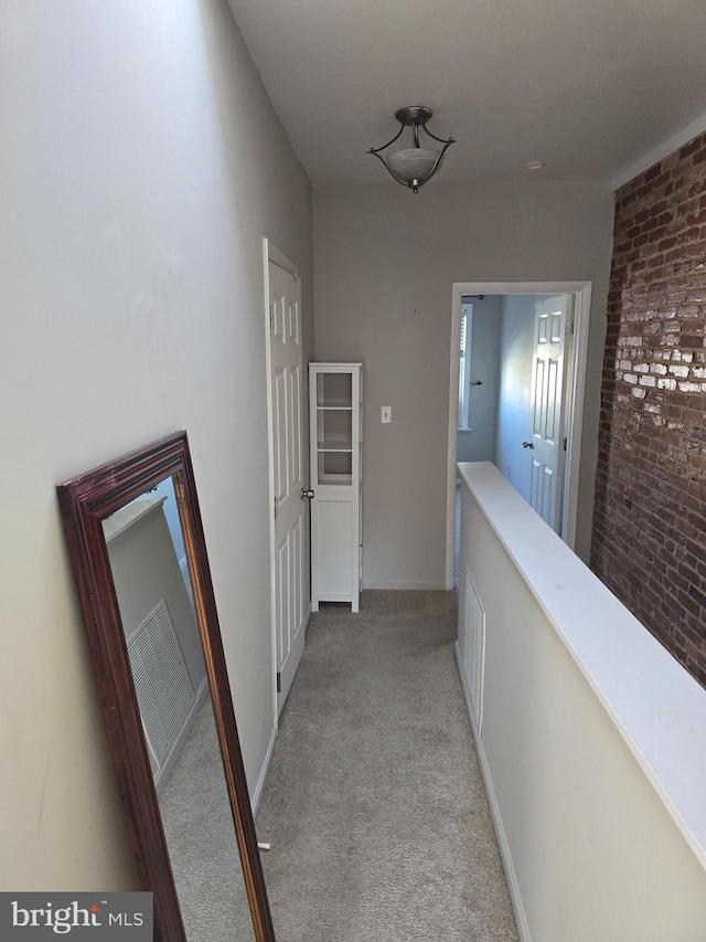 hall featuring light colored carpet and brick wall