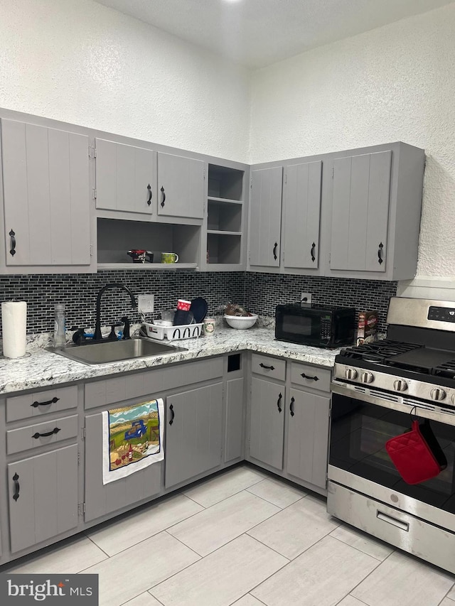 kitchen with sink, decorative backsplash, gray cabinets, and stainless steel stove