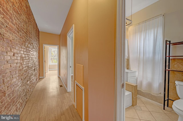 corridor featuring brick wall and light wood-type flooring