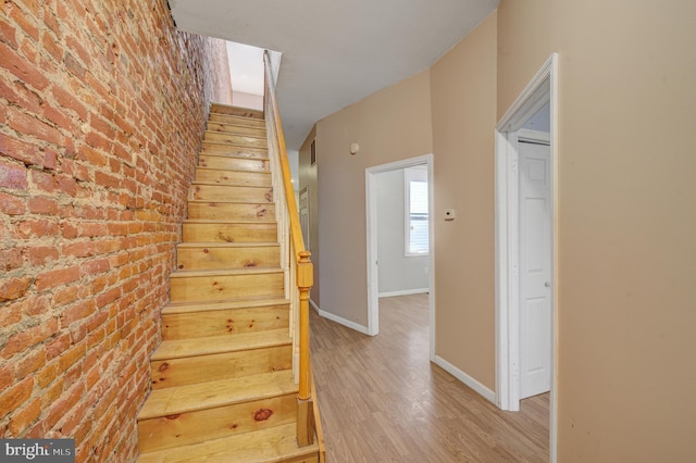 staircase with hardwood / wood-style flooring and brick wall