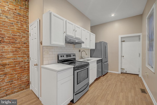 kitchen with light hardwood / wood-style flooring, white cabinetry, stainless steel appliances, and brick wall