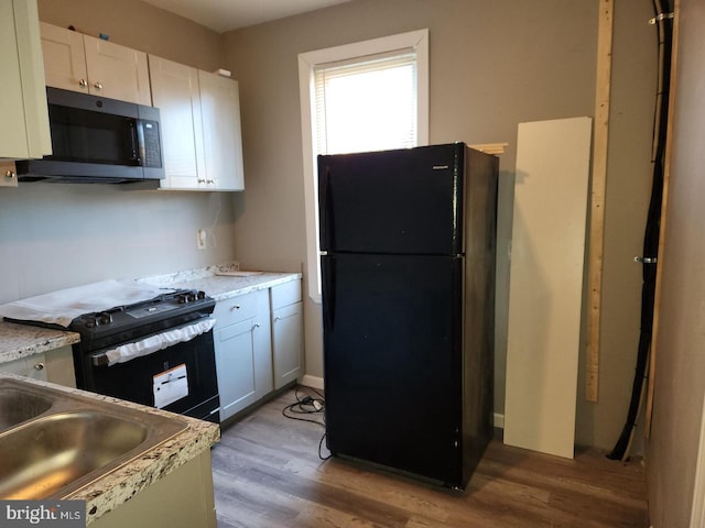 kitchen with hardwood / wood-style floors, sink, black appliances, and white cabinets