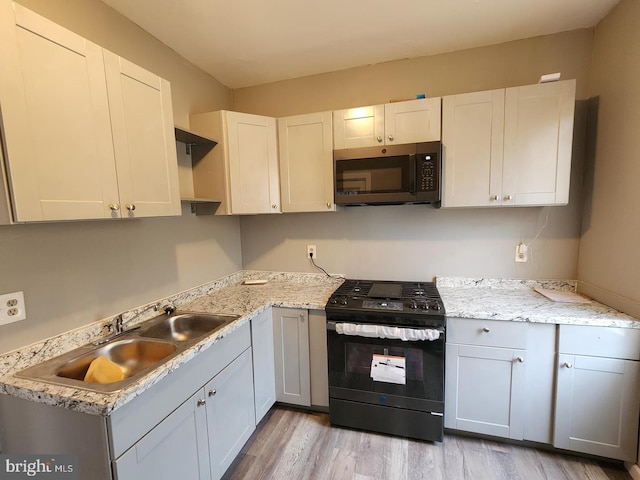 kitchen featuring sink, light stone counters, white cabinetry, black range with gas cooktop, and light hardwood / wood-style flooring