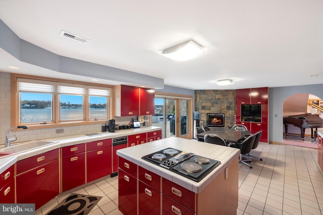 kitchen featuring sink, a center island, backsplash, black gas stovetop, and a fireplace