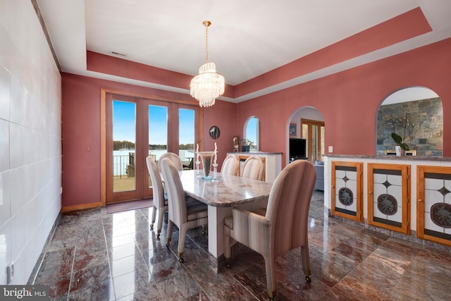 dining space featuring a raised ceiling, french doors, tile walls, and a notable chandelier