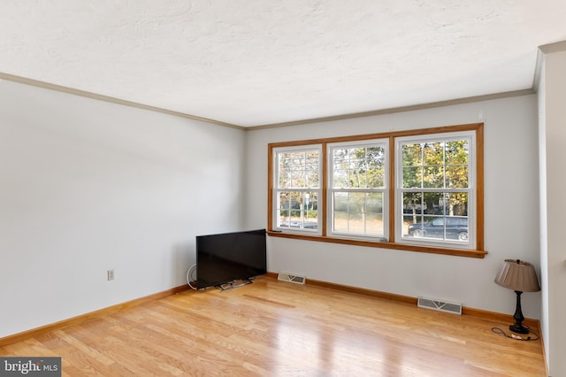 spare room with crown molding, a textured ceiling, a wealth of natural light, and hardwood / wood-style floors