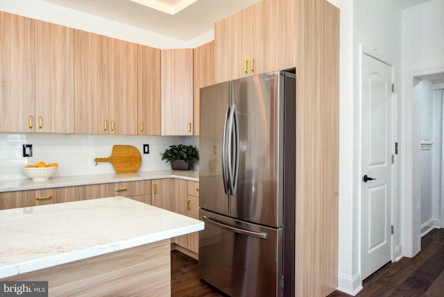 kitchen with light stone counters, stainless steel fridge, light brown cabinets, and dark wood-type flooring