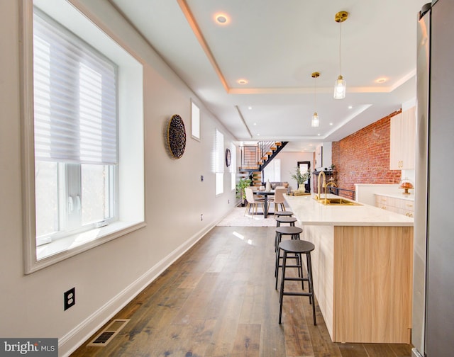 kitchen with dark hardwood / wood-style floors, pendant lighting, a healthy amount of sunlight, and a raised ceiling