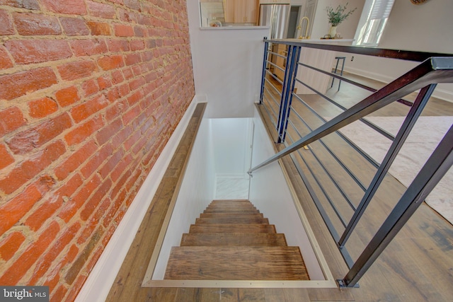 stairway featuring brick wall and wood-type flooring