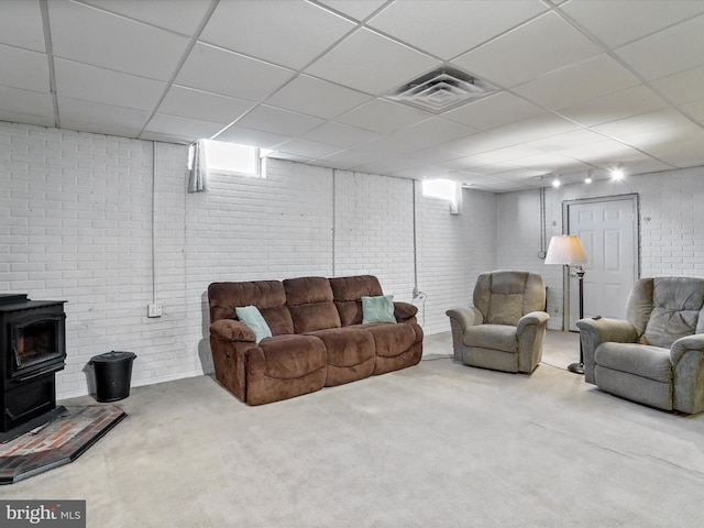 carpeted living room featuring a paneled ceiling and a wood stove