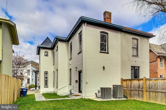 rear view of house featuring central air condition unit and a lawn