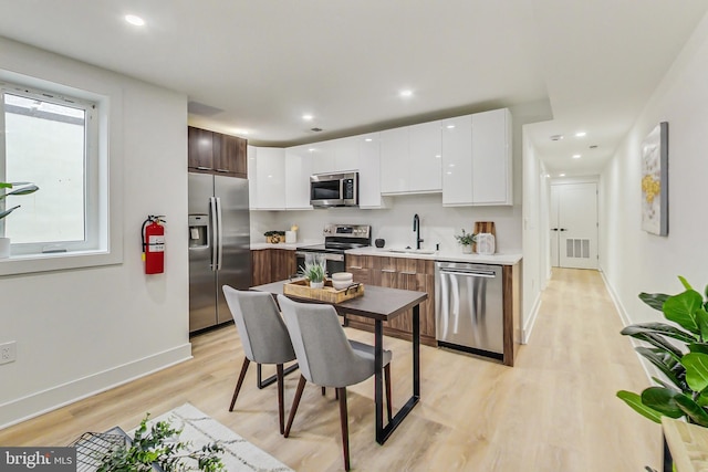 kitchen featuring stainless steel appliances, dark brown cabinetry, sink, light hardwood / wood-style floors, and white cabinets