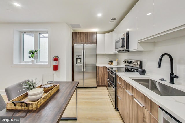 kitchen with butcher block countertops, white cabinetry, appliances with stainless steel finishes, sink, and light hardwood / wood-style floors