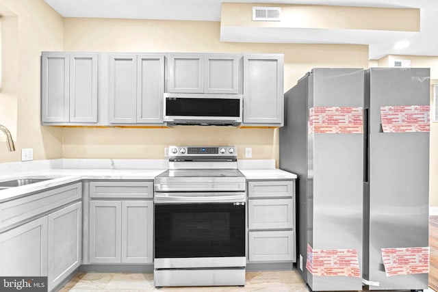 kitchen with a sink, gray cabinets, appliances with stainless steel finishes, and visible vents