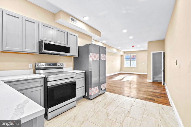 kitchen with appliances with stainless steel finishes, light stone counters, gray cabinetry, and light hardwood / wood-style floors