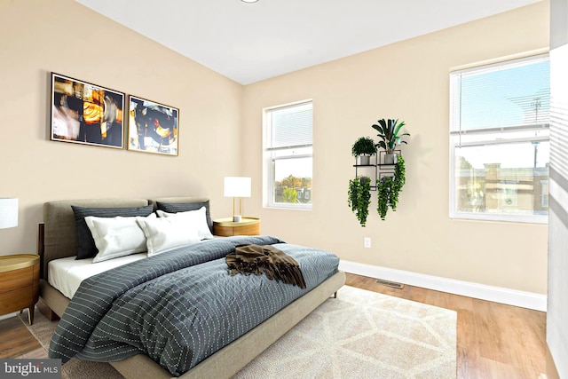 bedroom with multiple windows, wood finished floors, visible vents, and baseboards