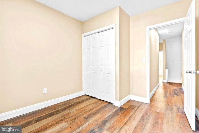 unfurnished bedroom featuring baseboards, wood finished floors, and a closet