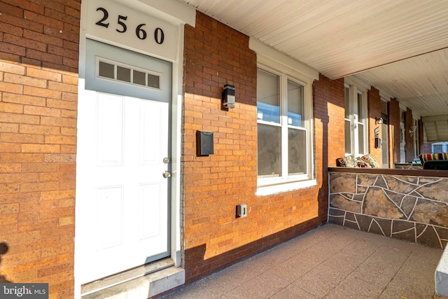 view of exterior entry with a porch and brick siding