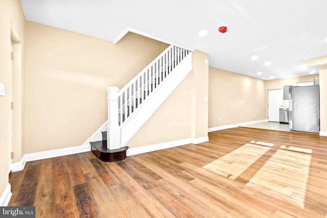 unfurnished living room featuring baseboards, stairway, light wood-style flooring, and recessed lighting