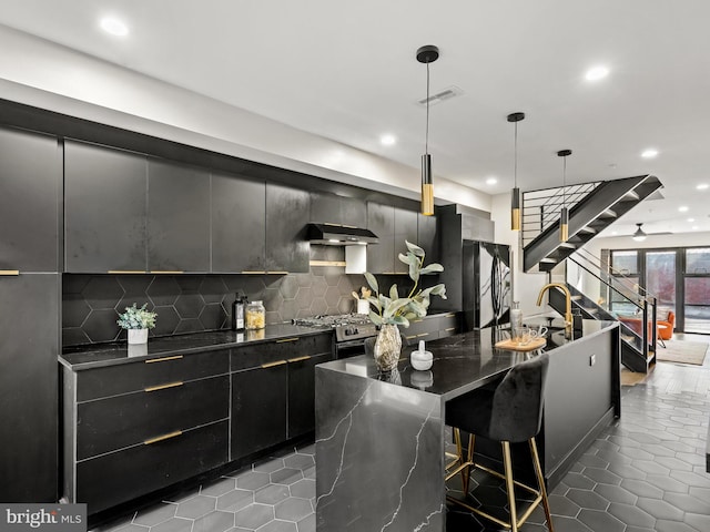 kitchen featuring a kitchen island, decorative backsplash, a breakfast bar area, black refrigerator, and decorative light fixtures